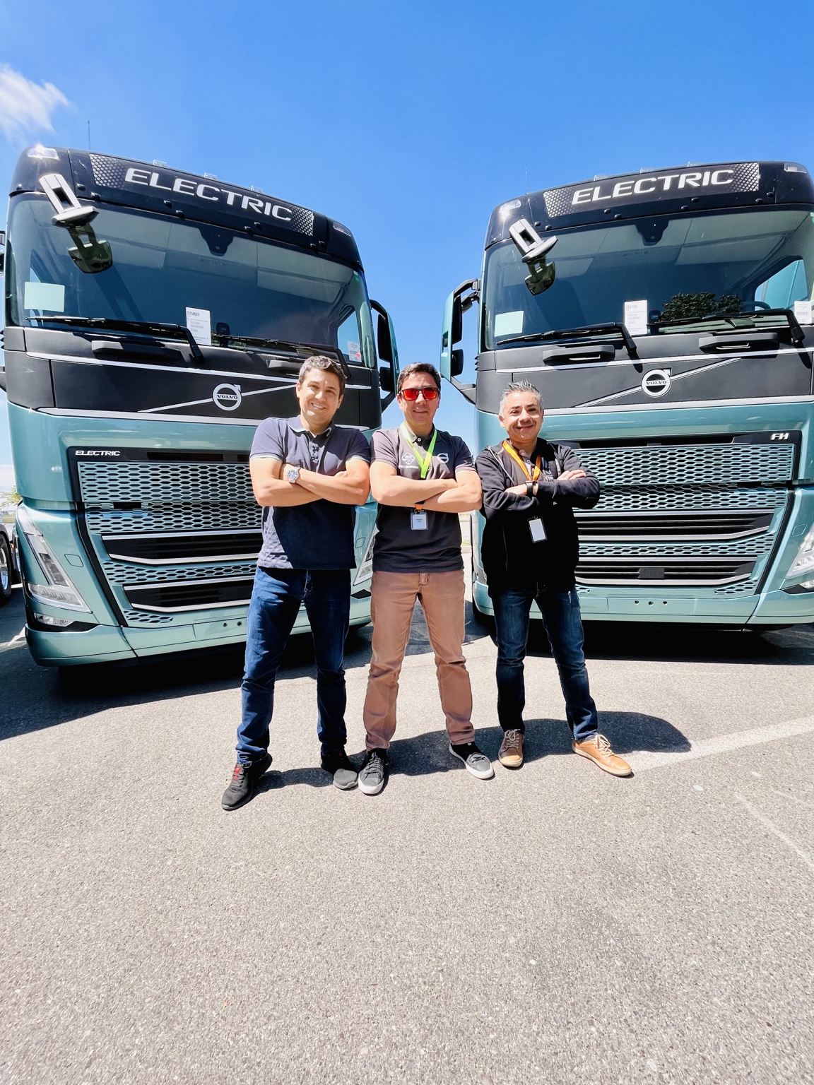 Tres personas junto a dos camiones eléctricos Volvo